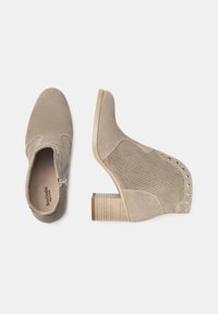 Bottines à talons beiges avec un dessus en suede texturé, des accents en maille et des clous en argent. Talon en bois épais avec des détails rayés.