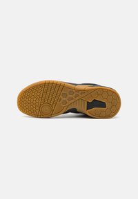 Black athletic shoe sole featuring a textured rubber design, hexagonal and patterned grip, with a tan central section and rounded accents.
