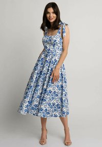 Sukienka midi w kwiatowy wzór w białym i niebieskim kolorze, z kwadratowym dekoltem, wiązanymi ramiączkami oraz rozkloszowanym dołem. Gładki, lekki materiał.