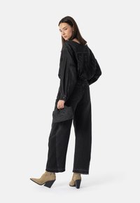 Czarna, oversize koszula dżinsowa z wyraźnymi napisami, zestawiona z czarnymi dżinsami z wysokim stanem i beżowymi botkami na obcasie. Mała, fakturowana czarna torebka.