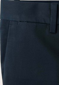 Pantalon bleu marine foncé en gros plan montrant la ceinture, la passants et la couture latérale en tissu tissé lisse.