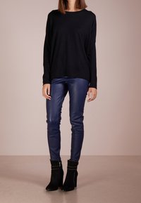 Svart långärmad tröja, blå byxor i faux läder och svarta ankelskoboots med silvernitar. Slät textur med en avslappnad passform.