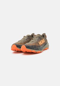 Green and black trail running shoes with orange accents, textured upper, lace closure, and rugged orange sole for traction.