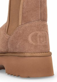 Stivale alla caviglia in suede marrone con pannello in tessuto liscio, parte superiore testurizzata e suola in gomma con righe, arricchita da un logo vicino al tallone.