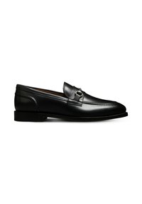 Mocassin noir en cuir à enfiler avec semelle plate, arborant une boucle en métal argenté décorative sur le dessus et des détails de couture visibles.