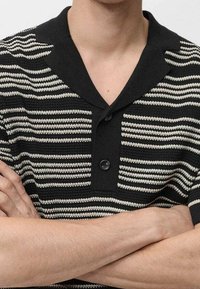 Mustat ja kerma valkoiset raitapaitapusero, jossa on huivi kaulus, kaulassa nappikiinnitys ja lyhyet hihat. Teksturoitu neulemateriaali.