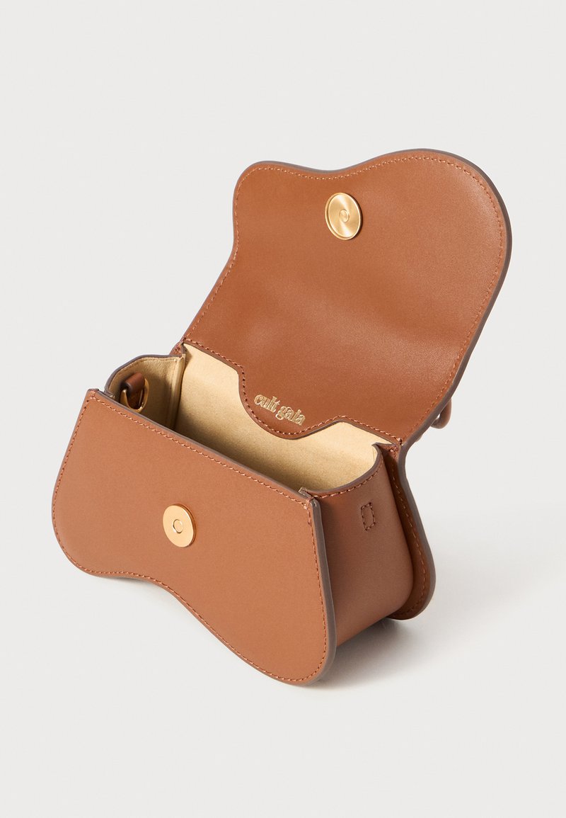 Sac en cuir marron au design arrondi, avec fermeture à pression métallique et doublure intérieure dorée. Présente une surface texturée et un branding subtil à l'intérieur.