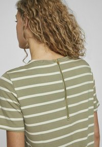 Koszulka w paski z jasnoszarym tłem i białymi paskami, krótki rękaw oraz zamek błyskawiczny z tyłu z złotym akcentem.