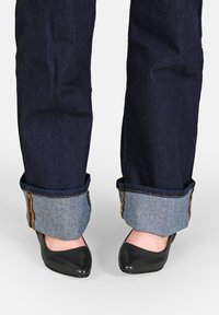 Jeans in denim blu scuro con risvolti che mettono in mostra un tessuto in denim più chiaro sottostante, abbinati a tacchi neri a punta.