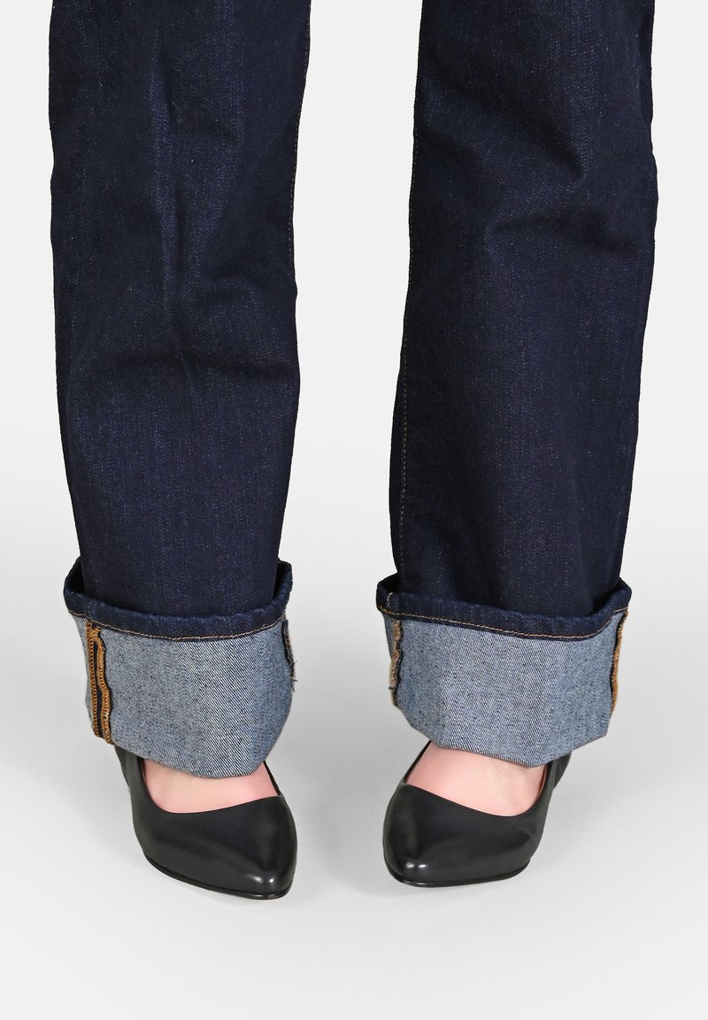 Jeans in denim blu scuro con risvolti che mettono in mostra un tessuto in denim più chiaro sottostante, abbinati a tacchi neri a punta.