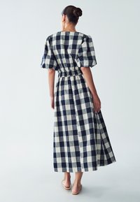 Maxime dress in navy and white checkered pattern. Features puffed sleeves, gathered waist, and a flowing skirt with a straight hem.