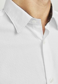 Camisa blanca de botones con un tejido texturizado, con un cuello de patrón oscuro en contraste y un cierre de un solo botón.