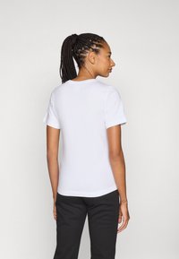 Witte T-shirt met korte mouwen en een ronde hals, zachte textuur en een relaxte pasvorm. De achteraanzicht toont een naadloos ontwerp. Gecombineerd met donkergekleurde broek.