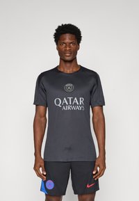 Czarna koszulka sportowa z krótkimi rękawami, z okrągłym logo i napisem "QATAR AIRWAYS" w szarym kolorze. Noszona z czarnymi szortami i niebieskimi akcentami.