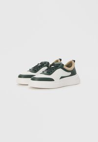 Green and white sneakers made of textured leather with a thick cream sole, featuring black laces and a tan inner lining.