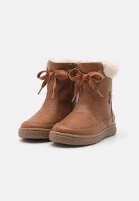 Braune Leder-Stiefel mit Knöchelhöhe und einem mit Fell gefütterten Schaft, ausgestattet mit einem seitlichen Reißverschluss, dekorativen Schleifen und strukturierten Gummisohlen.