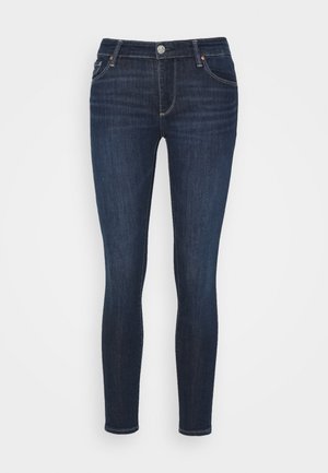 Tummansiniset skinny-farkut, joissa klassinen viiden taskun malli ja nappisuljin, esitetty yksiväristä vaaleaa taustaa vasten.