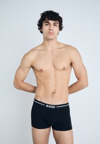 Black boxer briefs with a soft waistband featuring "BOSS" in white letters and gray accents. Material appears stretchy and form-fitting.
