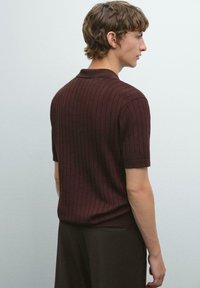 Brun ribbad kortärmad polo med krage, med en figurnära design och slät textur, bärs tillsammans med mörka byxor.