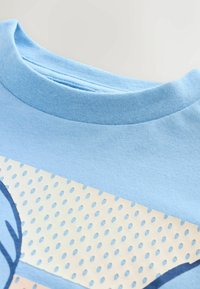 Vaaleansininen puuvillapaita, jossa on pyöreä pääntie, sileä pinta ja painettu kuvio, jossa on beigejä ja sinisiä yksityiskohtia sekä pistemäinen kuvio.