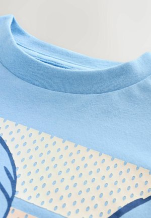 Hellblaues Baumwoll-T-Shirt mit rundem Halsausschnitt, glatter Textur und einem bedruckten Design mit einem gepunkteten Muster in Beige und blauen Akzenten.