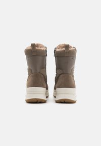 Bottines en suede marron avec un intérieur duveteux, présentant une fermeture éclair latérale et une semelle texturée blanche. Un tirant à l'arrière pour un enfilage facile.