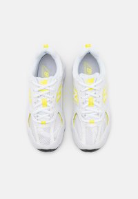 Vitaidiga sportskor med nätmaterial, gula accenter, rund design och en strukturerad sula med snörning och varumärke på sidorna.