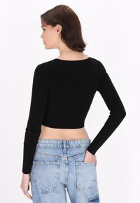 Fekete bordázott, hosszú ujjú cropped pulóver kerek nyakkivágással, világoskék, magas derekú, koptatott farmernadrággal párosítva. Minimális dizájn, minták nélkül.