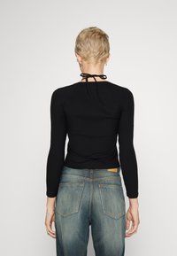 Haut noir à manches longues côtelé avec un design ajusté et un lien de fermeture au cou, associé à un jean en denim bleu avec des poches arrière.