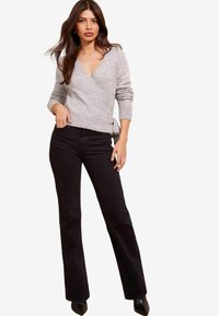 Grå omslagskoft med djup V-ringning, ribbade manschetter, tillsammans med svarta utsvängda jeans och spetsiga svarta klackar. Slät tygtextur.