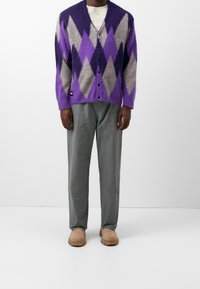 Cardigan argyle morado y gris con una textura esponjosa, delantero abotonado y mangas largas, combinado con pantalones grises y calzado beige.