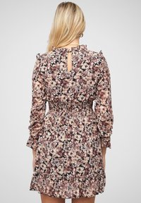 Kukava mekko tummasta kankaasta, jossa on pitkät hihat, röyhelökoristeet, vyötä ympäröivä vyötärö ja avonainen takapaneeli, sekä kerroksellinen röyhelöhelma.