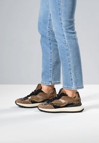 Baskets marron et noires avec un mélange de suède et de matériaux brillants, arborant des accents imprimés léopard et une semelle en caoutchouc blanche.