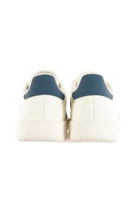 White sneakers with a smooth surface and blue heel accents. Features a rounded toe and a textured sole for grip. Minimalist design.