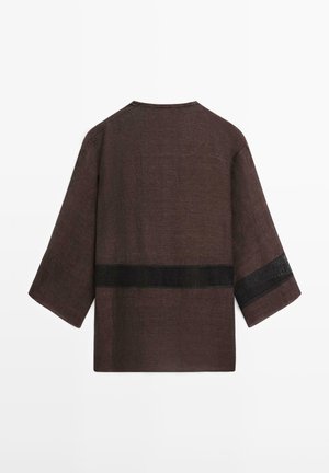 Hnědý volný top se tříčtvrtečními rukávy, s horizontálním černým síťovaným pruhem přes záda a jeden rukáv.