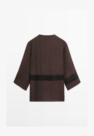 Hnědý volný top se tříčtvrtečními rukávy, s horizontálním černým síťovaným pruhem přes záda a jeden rukáv.