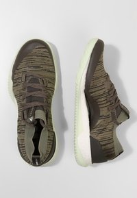 Scarpe sportive a maglia verde con design testurizzato, dotate di un tallone marrone scuro e una suola verde chiaro; includono lacci e branding sul lato.