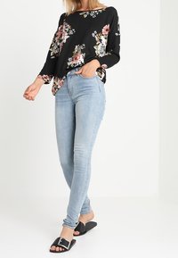 Musta kukallinen pitkähihaisten paita, joka on löysästi istuva, yhdistettynä vaaleansinisiin slim-fit-farkkuihin ja mustiin liukuviin sandaaleihin, joissa on solk yksityiskohta.