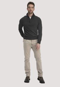 Dunkelgrauer Zip-Kragen-Pullover aus Strickstoff, kombiniert mit hellbeigen Jeans und dunklen Schnürstiefeln. Die Passform der Kleidung ist lässig mit einer entspannten Silhouette.