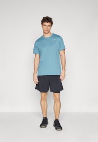 Light blue crew-neck athletic t-shirt with short sleeves and a white logo, paired with black shorts and black athletic shoes.