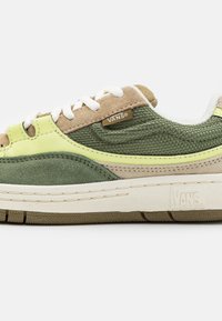 Des baskets Vans avec un mélange de suède vert et beige, des tissus texturés, des lacets blancs et une semelle en caoutchouc avec un motif de rainure.