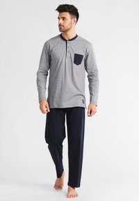 Chemise grise à manches longues avec col et poche navy, dotée d'une patte de boutonnage. Accompagnée d'un pantalon de détente navy, le tout en mélange de coton.