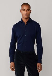 Donkerblauwe lange mouwen shirt met een button-down kraag, gemaakt van gladde stof, gecombineerd met zwarte corduroy broek. Geen patronen of accenten zichtbaar.