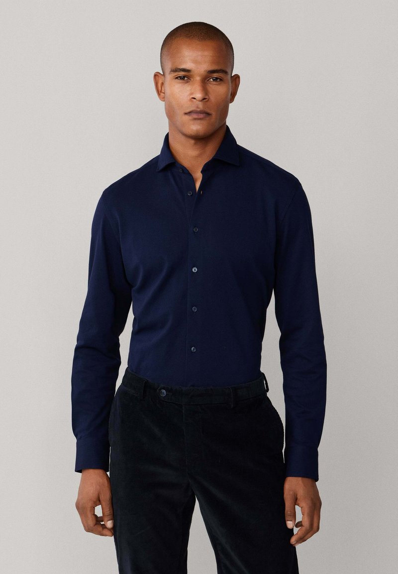Donkerblauwe lange mouwen shirt met een button-down kraag, gemaakt van gladde stof, gecombineerd met zwarte corduroy broek. Geen patronen of accenten zichtbaar.