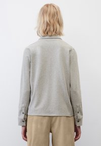 Camicia a maniche lunghe in cotone grigio con colletto, polsini abbottonati e vestibilità rilassata, abbinata a pantaloni beige chiaro.