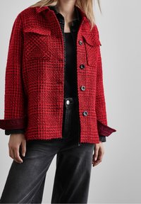 Red, textured button-up jacket with two front pockets and black buttons. Includes a contrasting maroon inner lining and collar detail.