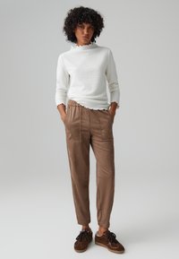 Waffle-knit white long-sleeve top with scalloped trim, paired with caramel-colored, textured elastic-waist trousers and brown sneakers.