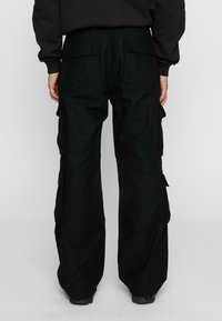 Czarne spodnie cargo o luźnym kroju, z kieszeniami po bokach, z guzikami i teksturowanym materiałem. Elastyczne mankiety przy kostkach.