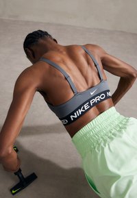 Nike Pro sportinis liemenukas pilkos spalvos, su reguliuojamomis petnešomis ir juodu juostu. Su laisvomis, ryškiai žaliomis sportinėmis kelnėmis. Atlieka atsilenkimus.