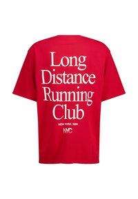 Punainen puuvillapaita rentoa kokoa, jossa on rohkea valkoinen teksti "Pitkän matkan juoksuklubi" ja "New York 1989" selässä.